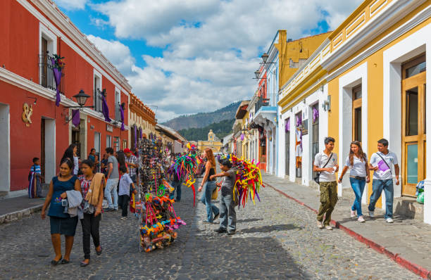 Antigua Main Street Cityscape Cityscape of the main street of Antigua on a summer day with tourists and sellers with the multi colored colonial style architecture of the city, Guatemala, Central America. agua volcano photos stock pictures, royalty-free photos & images