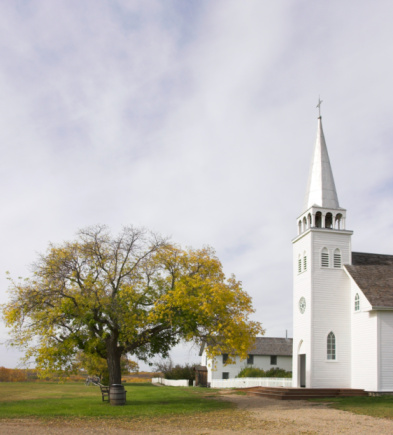 White country Baptist church surrounded by autumn colors in New England. White clouds and blue sky background.