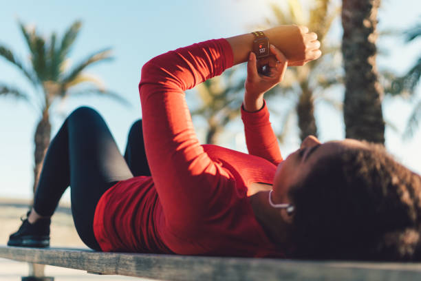 Sportswoman checking pulse on smartwatch Mixed race woman resting at park bench and tracing pulse on smartwatch tracker stock pictures, royalty-free photos & images