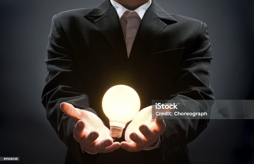 A businessman with a lit lightbulb in his hands a man pointing to the illuminated bulb Achievement Stock Photo