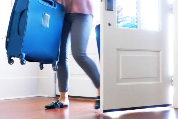 istock Woman carrying luggage into home ar front door. 895100740