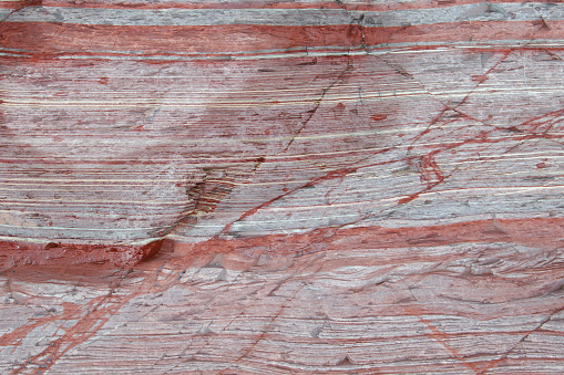 Close up of mostly red sediment layers in a rock formation. Photographed; Clovelly, Devon, UK. December 2017.
