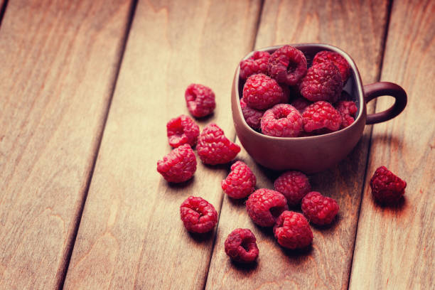 istock Raspberries in a cup and on a wooden table 895135474