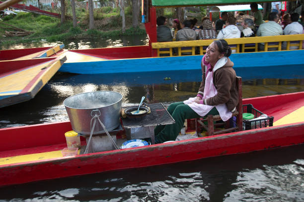 Xochimilco trajineras Xochimilco, Mexico City, Mexico - 2017: A woman sells local food on a trajinera (a type of local boat) at a city canal trajinera stock pictures, royalty-free photos & images