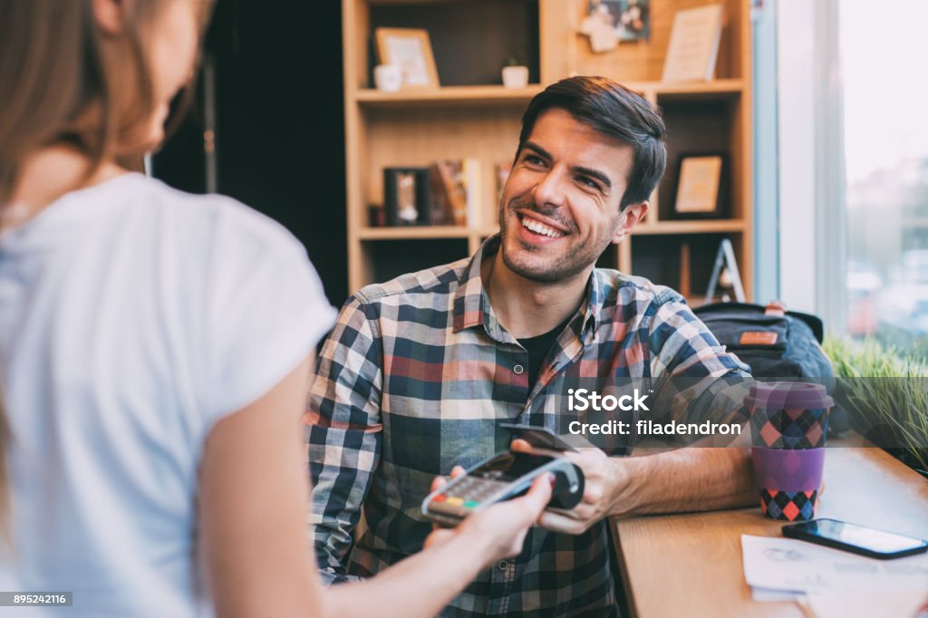 Man paying via smart phone Young man paying via smart phone to a waiter at the cafe. Credit Card Stock Photo