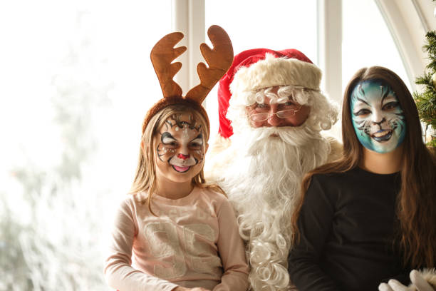 Portrait of two little girls that have Christmas motives painted on their faces. They are sitting in Santa's lap.
