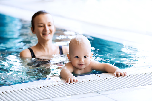 Mother teaching baby to swim. Portrait of a charming 11 months child in the classroom in a swimming pool. Healthy Family Life.