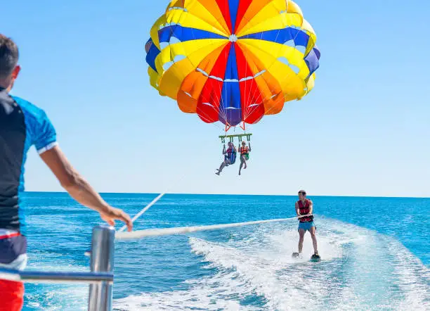 Happy couple Parasailing in Dominicana beach in summer. Couple under parachute hanging mid air. Positive human emotions, feelings, family. Young man glides on water skiing on the waves.Healthy lifestyle.