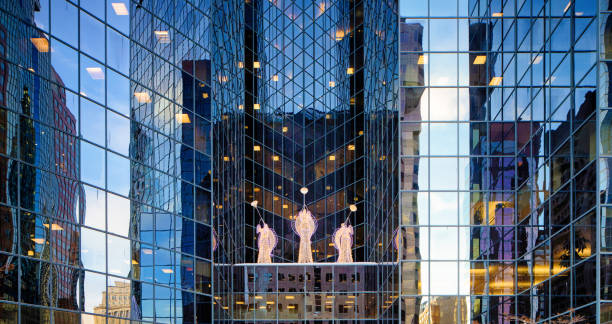 Angel Christmas decorations among shiny office building windows reflecting a December sunset. There are three angels blowing trumpets.
