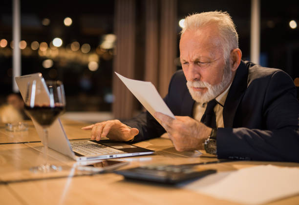Senior man working late and struggling to read a document.