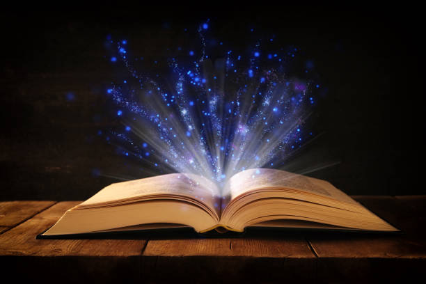 istock image of open antique book on wooden table with glitter overlay. 895385192