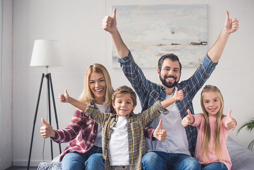 portrait of happy family showing thumbs up and looking at camera at home