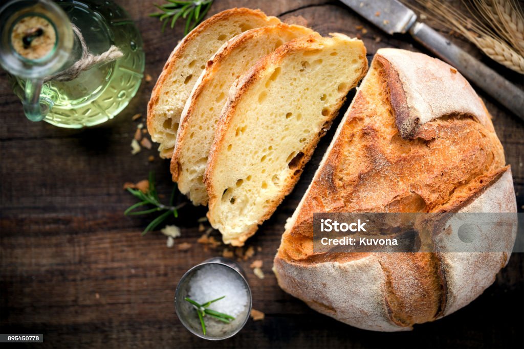 Loaf of rustic homemade bread Rustic loaf of homemade bread served with olive oil, rosemary and salt on dark wooden table. Overhead view Bread Stock Photo