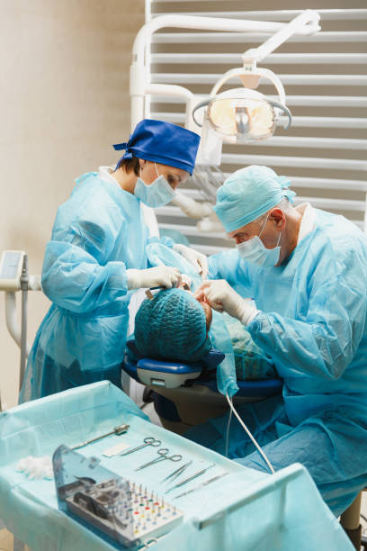 균일 하 고 여성 도우미에서 남성 오래 된 전문 치과 의사 현대 도구 장비 클리닉 빛 사무실에 여자 환자의 작업 설치 치과 임 플 란 트 치아를 수행 하는 데 도움이 됩니다. - sewing stitches thread surgery 뉴스 사진 이미지