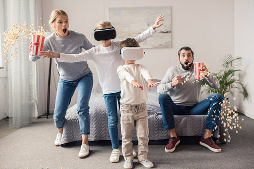 parents with pop corn watching kids playing in vr headsets at home