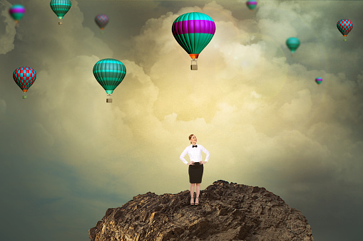 Businesswoman on cliff looking up at flying hot air balloons