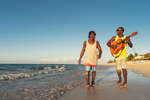 Two cuban friends having fun in the beach with his guitar. Friendship concept.