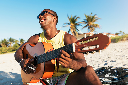 Young cuban man having fun in the beach with his guitar. Friendship concept.