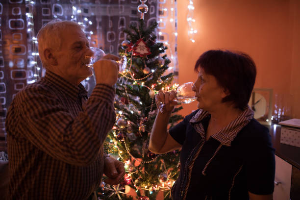 coppia senior che beve champagne davanti all'albero di natale - wine christmas alcohol evening ball foto e immagini stock