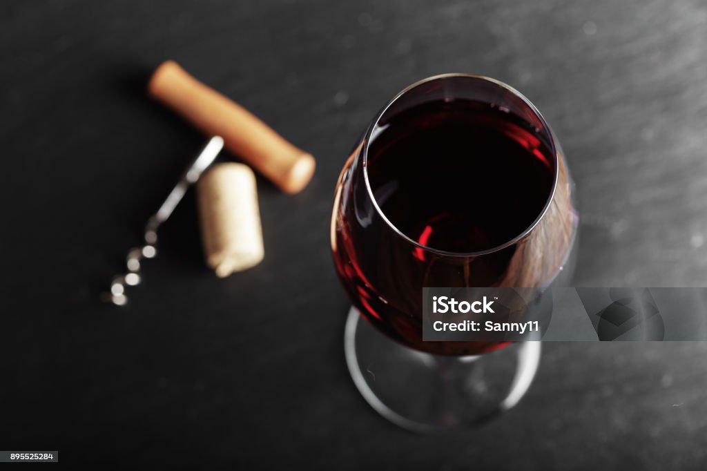 wine glass of red wine with a corkscrew. wine glass of red wine with a corkscrew. On a black wooden background. Wine Stock Photo