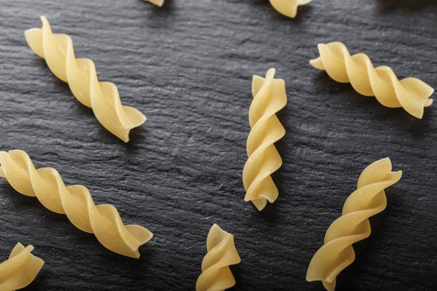 istock scattered of Rotini corkscrew pasta  on black stone table, top view. 895525446
