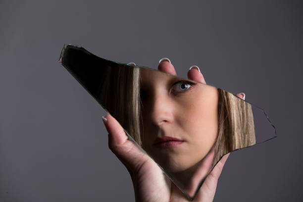 Woman looking at her face in a shard of broken mirror stock photo