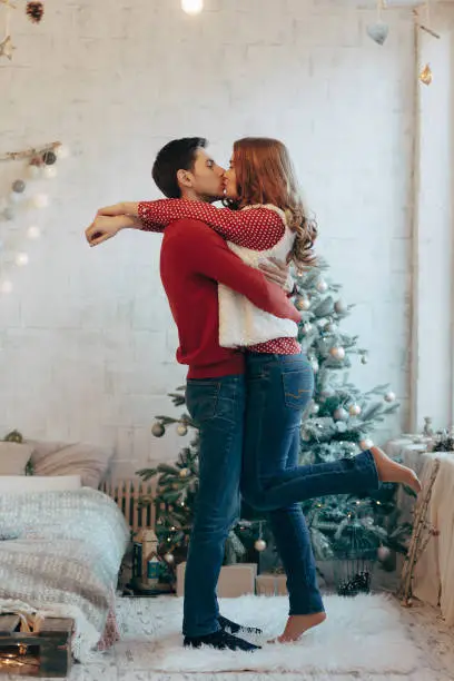 Picture showing young couple hugging and kissing over Christmas tree, full length