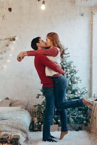 Picture showing young couple hugging and kissing over Christmas tree, full length