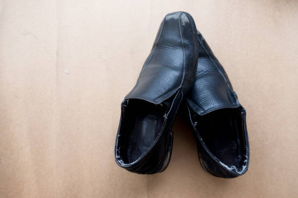 istock Old pair of used black leather shoes on brown background, top view 895539430