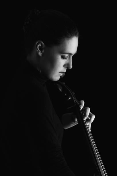 istock Beautiful brunette playing a cello with selective light in black dress artistic conversion 895557238