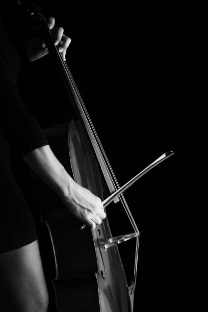 istock Beautiful brunette playing a cello with selective light in black dress artistic conversion 895557370