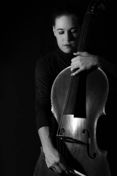 istock Beautiful brunette playing a cello with selective light in black dress artistic conversion 895559436