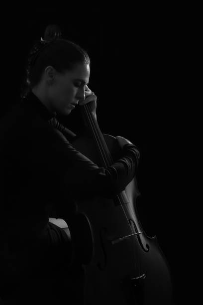 istock Beautiful brunette playing a cello with selective light in black dress artistic conversion 895561972