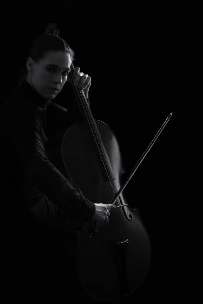 istock Beautiful brunette playing a cello with selective light in black dress artistic conversion 895563052