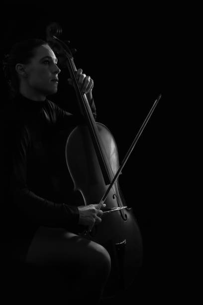 istock Beautiful brunette playing a cello with selective light in black dress artistic conversion 895563570
