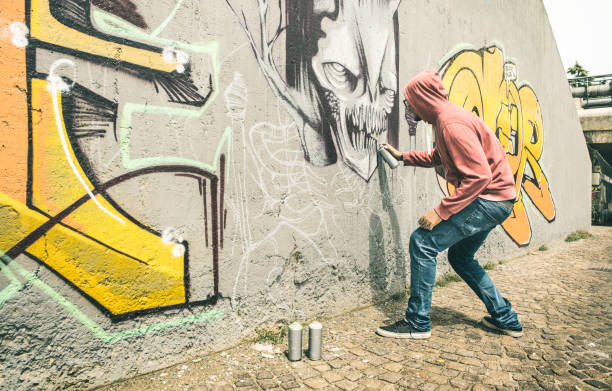 street artist painting colorful graffiti on generic wall - modern art concept with urban guy performing and preparing live murales with multi color aerosol spray - contrast retro vintage filter - graffiti men wall street art imagens e fotografias de stock