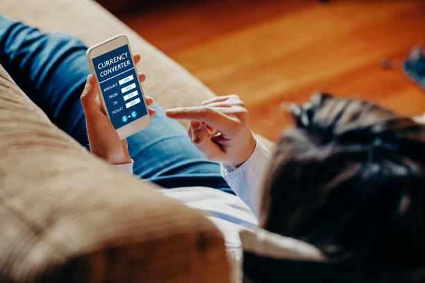 istock Woman using a mobile phone currency converter while sitting at home. 895576734