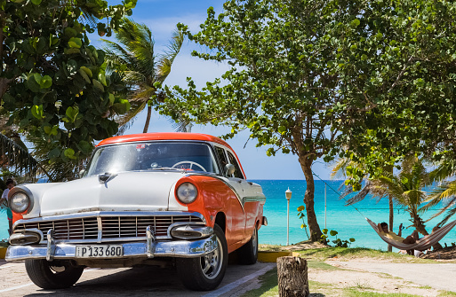 Varadero Cuba - June 24, 2017: HDR - Parked american white orange Ford Fairlane vintage car in the front view and with a relaxed cuban man on the beach in Varadero Cuba - Serie Cuba Reportage
