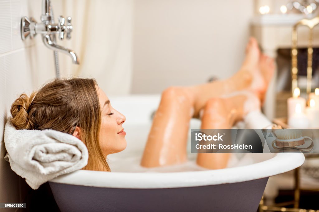 Woman bathing at the retro bathroom Young woman relaxing in the beautiful vintage bath full of foam in the retro bathroom decorated with candles Bathtub Stock Photo