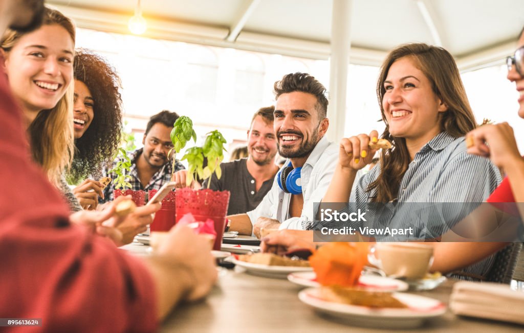 Friends group drinking cappuccino at coffee bar restaurant - People talking and having fun together at fashion cafeteria - Friendship concept with happy men and women at cafe - Warm vintage filter Friendship Stock Photo