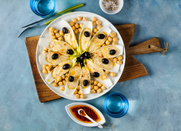 The leaves of Belgian endive with hummus, chickpeas and black olives. With strong olive oil of red pepperoncino. Modern delicious food for vegetarians and gourmets.