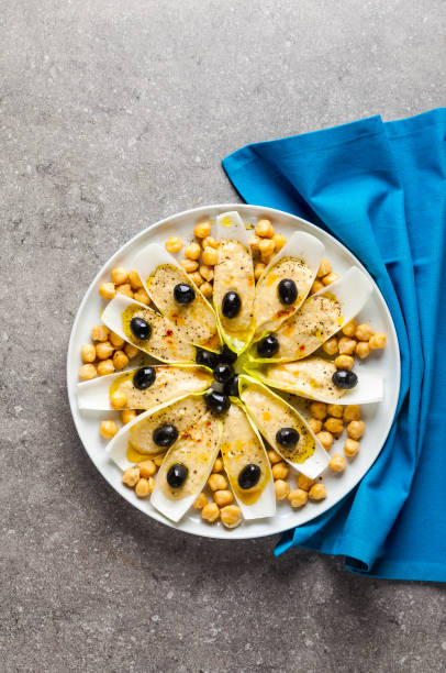 The leaves of Belgian endive with hummus, chickpeas and black olives. With strong olive oil of red pepperoncino. Modern delicious food for vegetarians and gourmets.