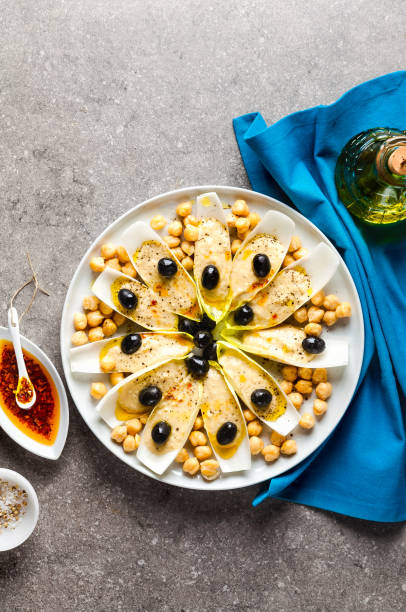 The leaves of Belgian endive with hummus, chickpeas and black olives. With strong olive oil of red pepperoncino. Modern delicious food for vegetarians and gourmets.