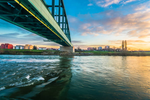Aerial drone view of multiple bridges spanning the Sava River in Zagreb, Croatia, captured at sunset. The image highlights the city's infrastructure, the flowing river, and the dramatic sky, creating a visually stunning and dynamic scene.