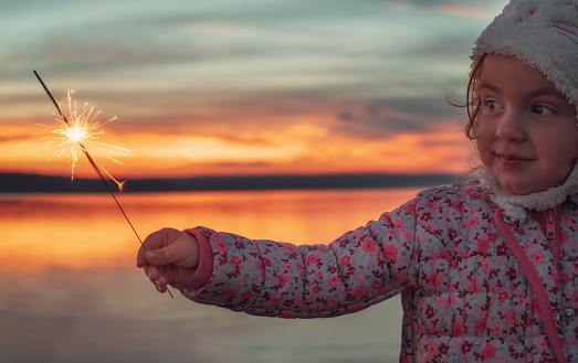 Beautiful girl with sparklers on the lake at sunset.