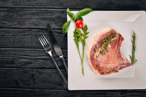 istock Raw veal steak on a plate. On a wooden background. Top view. Free space for text. 895660236