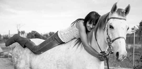 Young woman poses outdoor with her horse, in a shining day, in Spain. Se cuddles the horse.