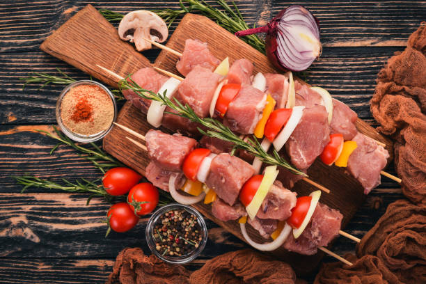 istock Raw kebab from meat on a wooden background with vegetables. Top view. Free space for text. 895672200