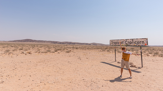 Rehobot, Namibia - august 30, 2016: One person with outstretched arms at Tropic of Capricorn signpost in the Namib Desert, Namibia, Africa.