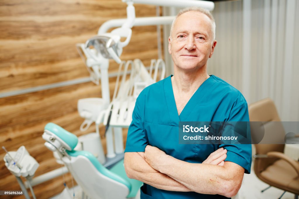Dentist in clinics Mature dentist in uniform crossing his arms on chest while looking at camera Dentist Stock Photo